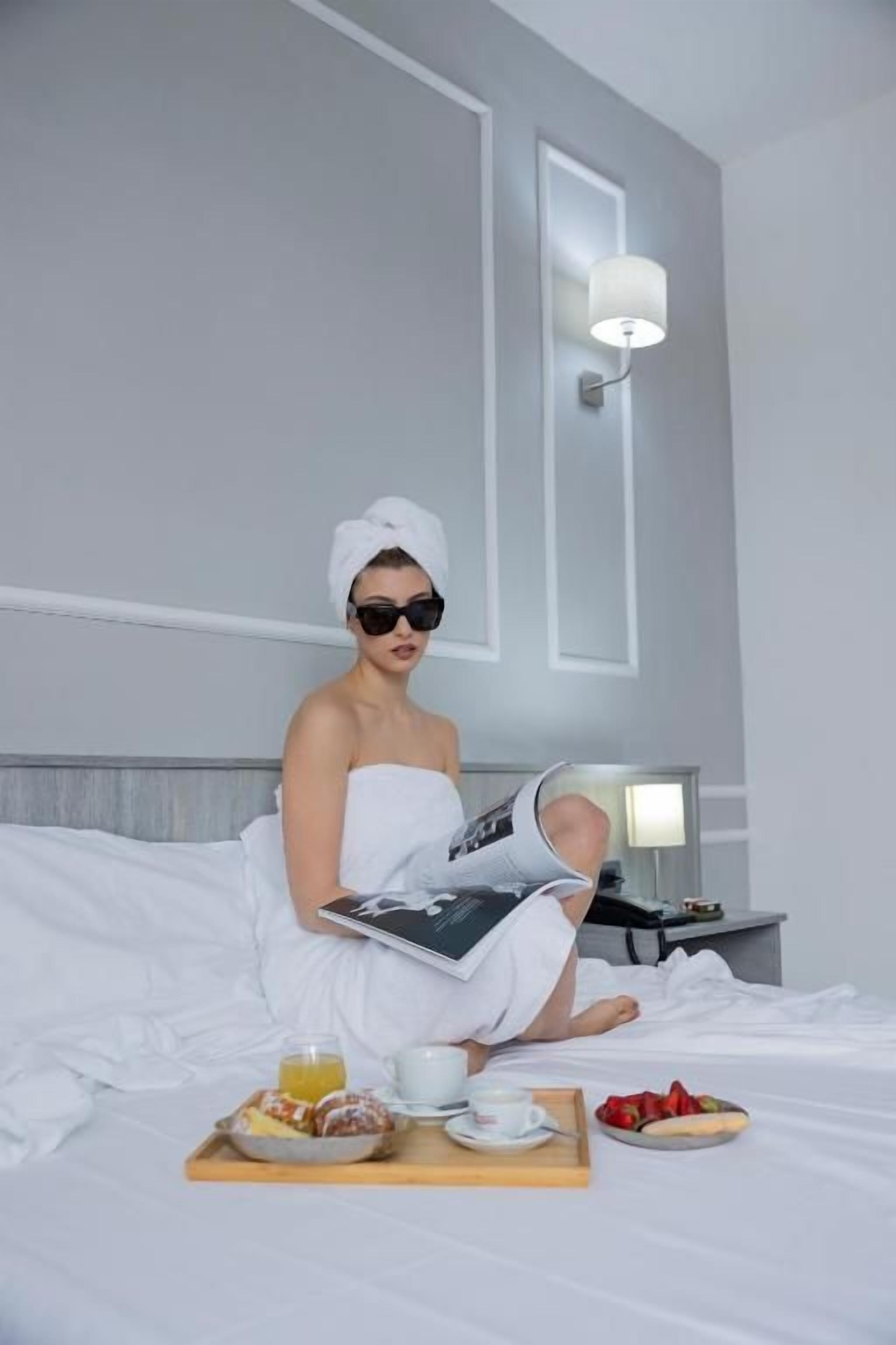 A person sitting on a bed with a tray of breakfast items, a cup, and a book.