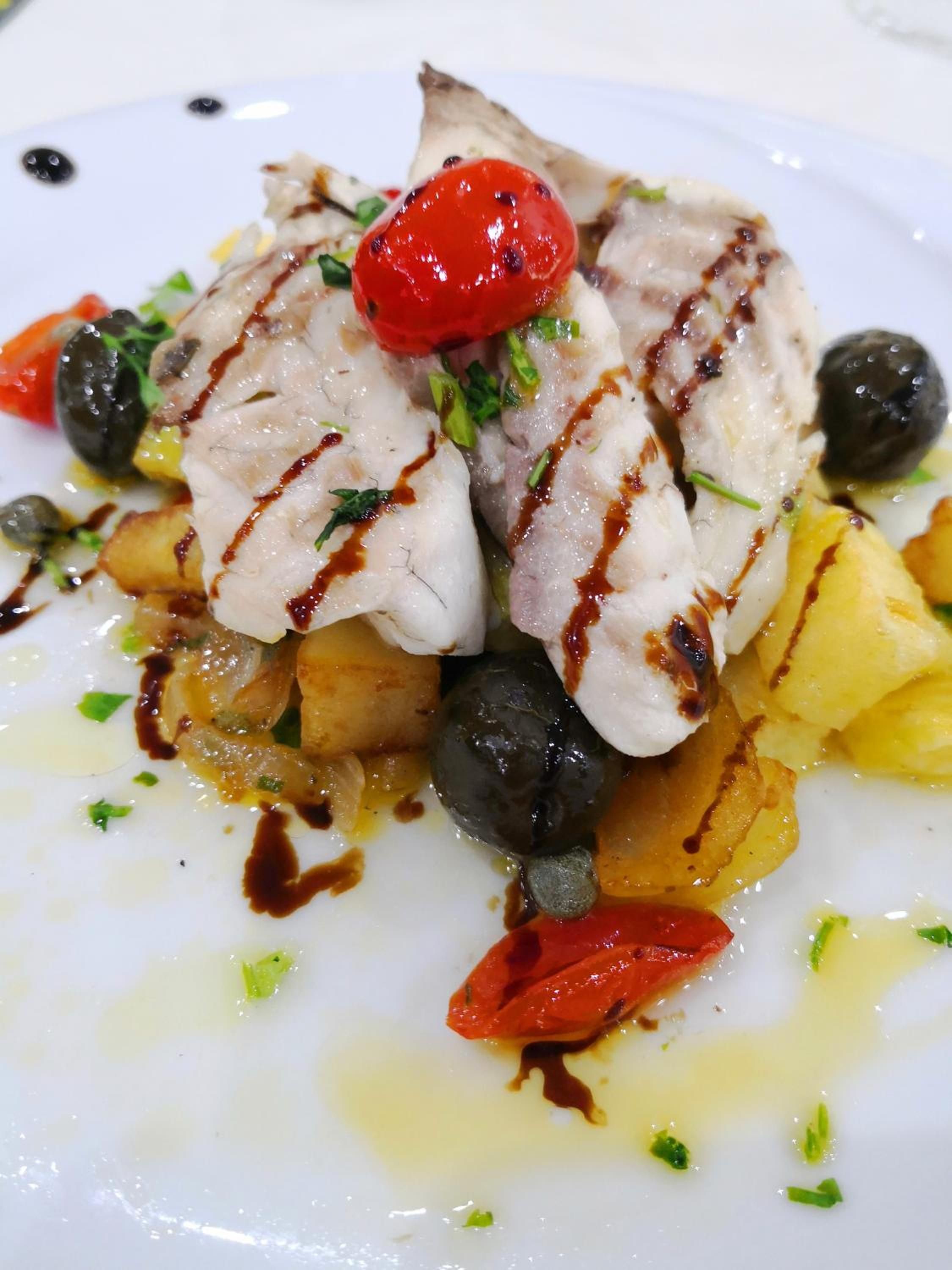 A plate of food with grilled fish, potatoes, olives, and cherry tomatoes.