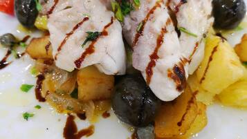 A plate of food with grilled fish, potatoes, olives, and cherry tomatoes.