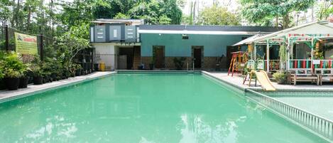A swimming pool with a slide, surrounded by greenery and a building with a green roof.