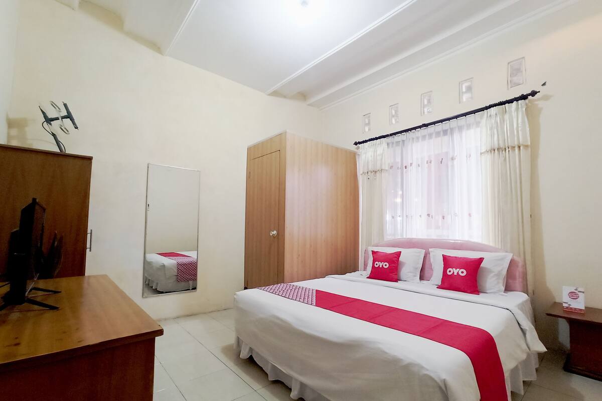 A bedroom with a bed, a wooden wardrobe, a mirror, and a desk.