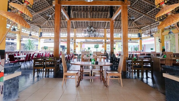 Un restaurante espacioso con techos altos, vigas de madera y varias áreas de comedor. Las mesas y sillas están dispuestas para grupos, con una zona central para celebraciones más grandes.