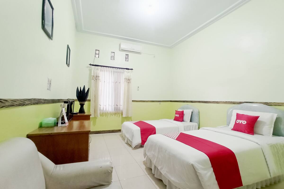 A hotel room with two beds, a desk, a chair, and a window with curtains.