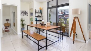 A modern dining area with a wooden table and benches, a black metal frame, and a view of a cityscape through large windows. - Flatrock 608 (Cape Town)