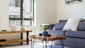 A modern living room with a grey sofa, a wooden coffee table, and a blue vase with a plant. - Flatrock 608 (Cape Town)