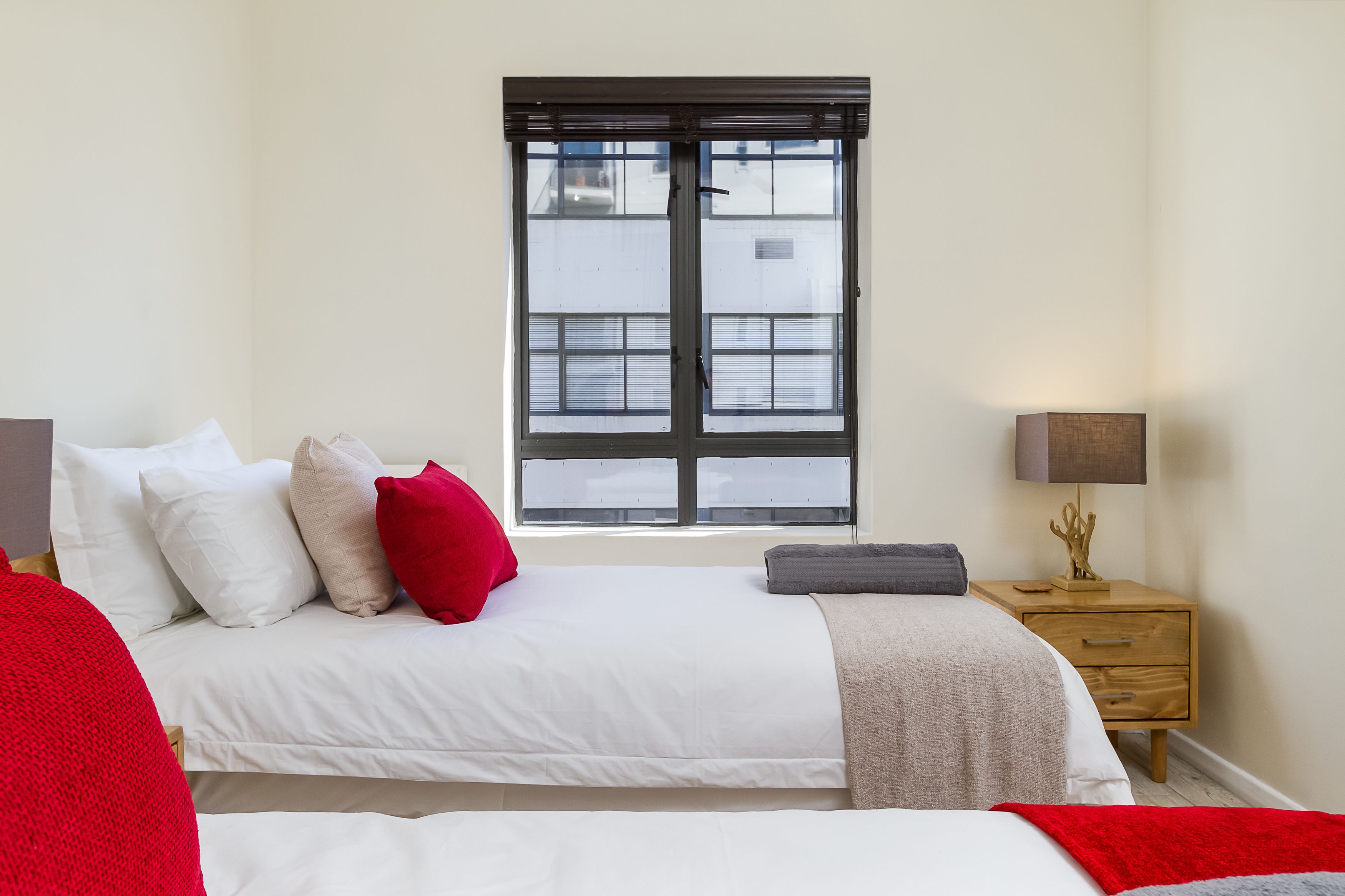 Un dormitorio con cama, almohadas, una mesita de noche, una lámpara y una ventana.