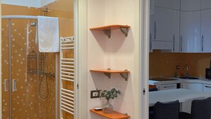 A compact kitchen with white cabinets, a dining area with two chairs, and a shower with a glass door. - Fiuggi Apartment (Milan)