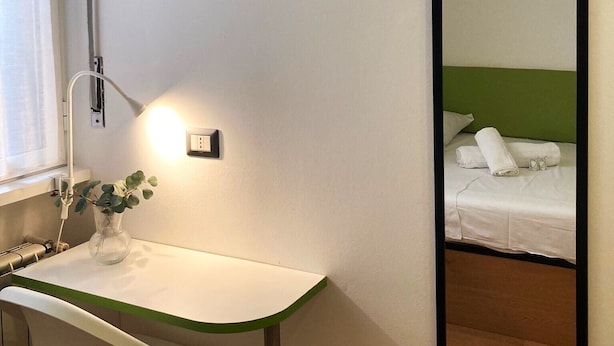 A hotel room with a white desk, a mirror, and a bed with green headboard. - Fiuggi Apartment (Milan)