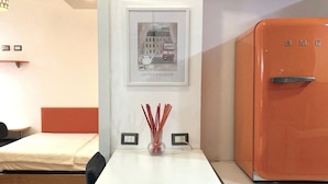 A hotel room with a white table, a framed picture of a cityscape, a small vase with red sticks, and an orange refrigerator. - Fiuggi Apartment (Milan)