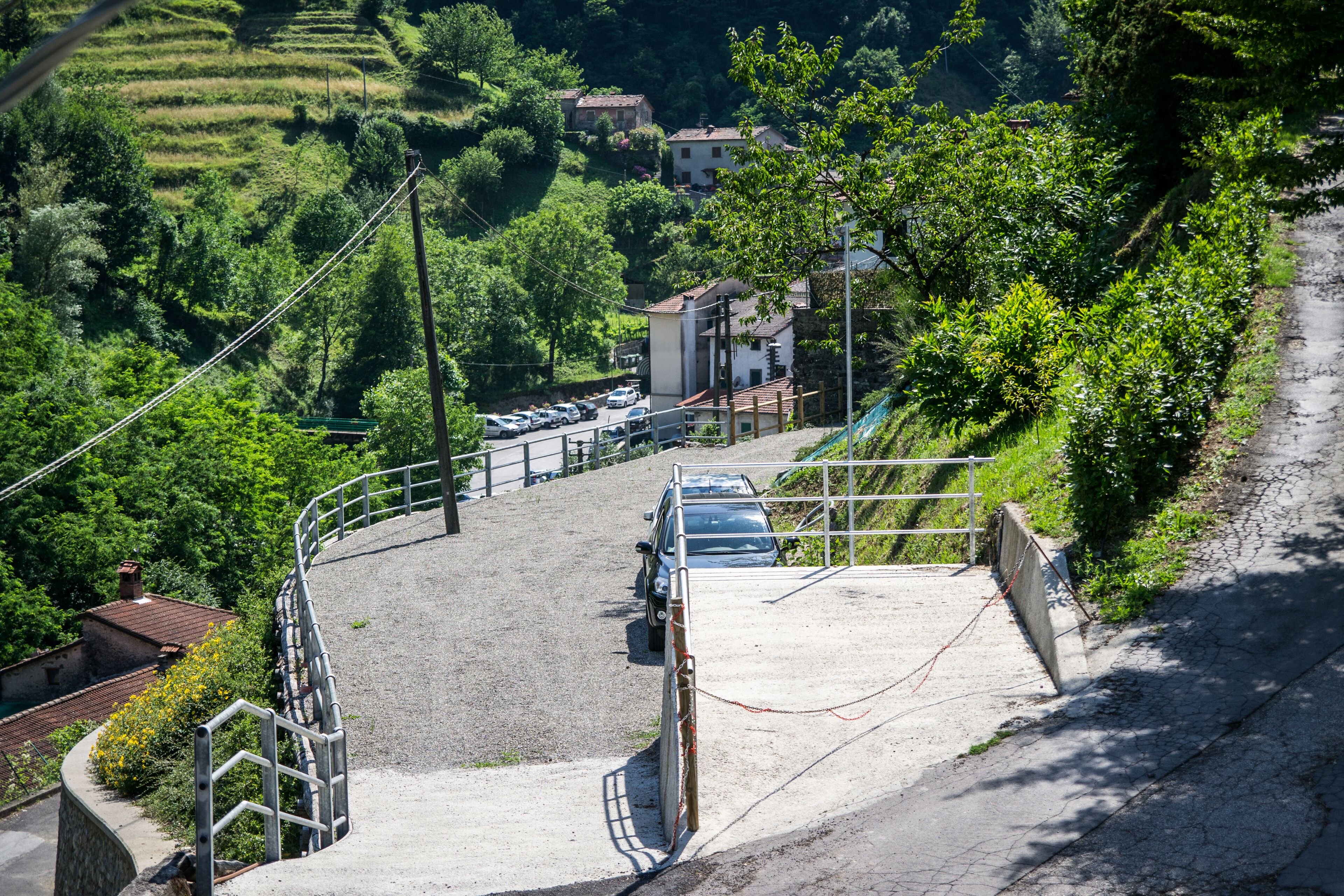 A parking area with cars, a staircase, and a view of terraced fields and buildings.