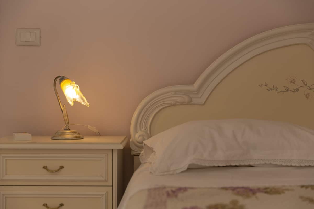 Een slaapkamer met een bed, nachtkastje, lamp en lichtschakelaar.