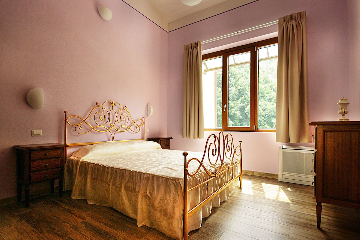 Een slaapkamer met een houten bed, nachtkastje, dressoir en een raam met gordijnen.