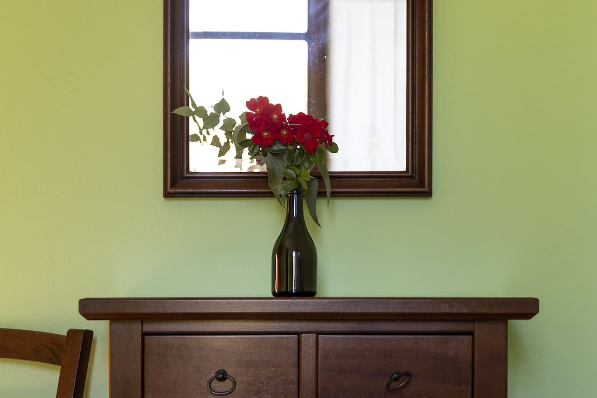 Een houten dressoir met een vaas rode bloemen erop, een spiegel erboven en een bed met een decoratief sprei.