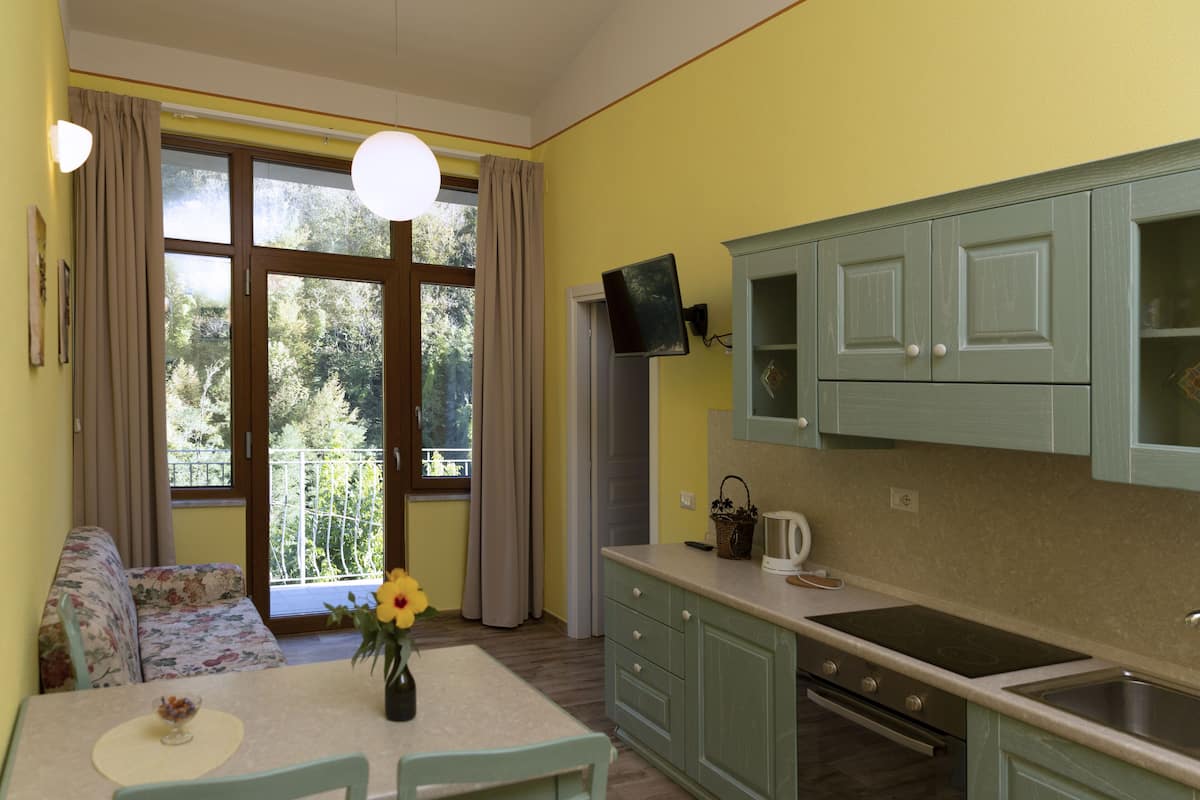 Een keuken met groene kastjes, een eettafel met stoelen, een bloevas en een raam met gordijnen.