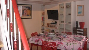 A dining area with a table set for four, surrounded by red chairs, a television mounted on the wall, and a bookshelf with various items. - Sansone apartment (Portoferraio)