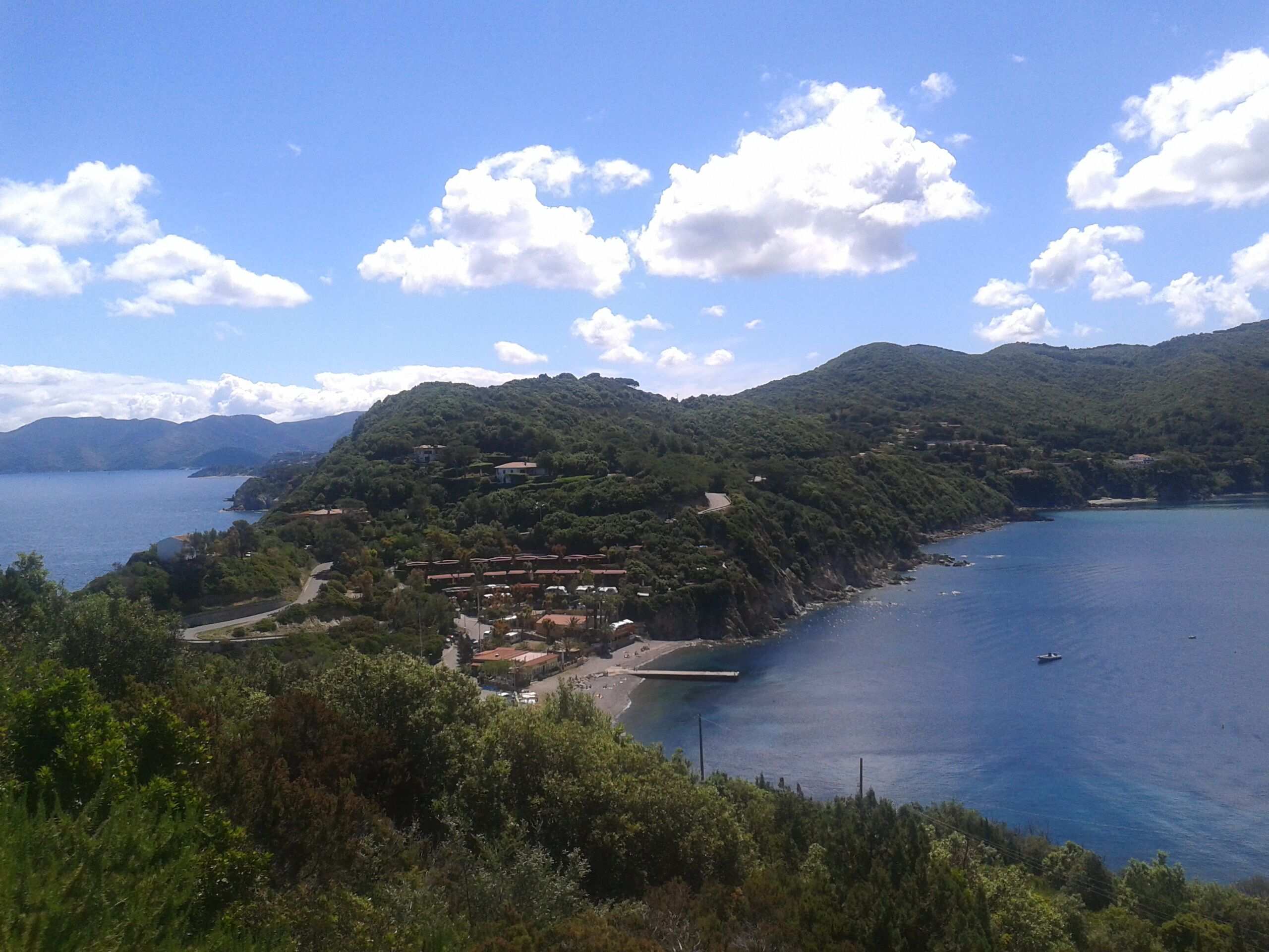 Une zone côtière comprenant un petit village, un quai et offrant une vue dégagée sur la mer et les montagnes.
