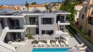 A modern building with a rooftop pool, lounge chairs, and umbrellas. - Athina Suites Platanias (Platanias)