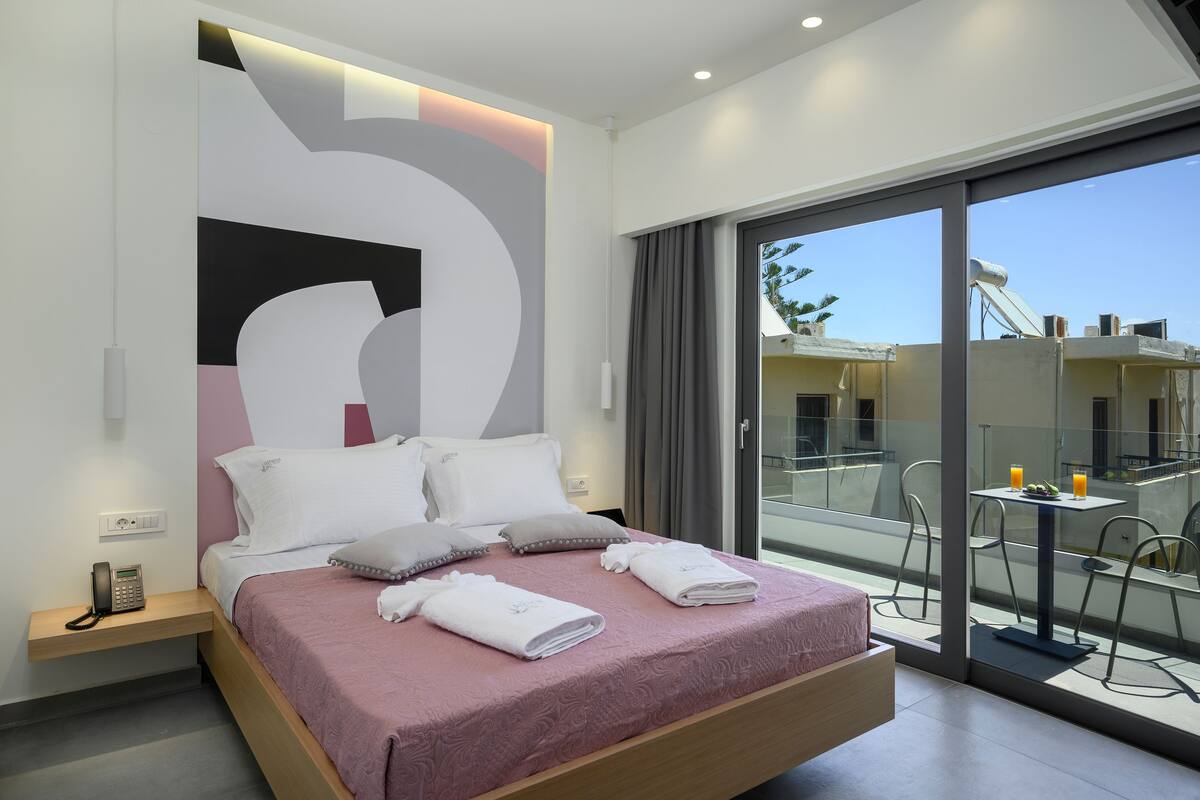 Una habitación de hotel moderna con una cama grande, un teléfono en la mesita de noche y un balcón con mesa y sillas.