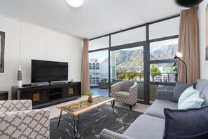 A modern living room with a large TV, comfortable seating, and a view of a cityscape through large windows. - Flatrock 703 (Cape Town)