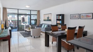 A modern living room with a dining area, large windows, and a view of buildings. - Flatrock 703 (Cape Town)