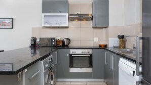 A modern kitchen with grey cabinets, a built-in oven, a dishwasher, and a coffee maker. - Flatrock 703 (Cape Town)