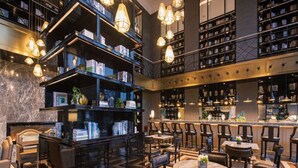 Una biblioteca moderna amb diversos nivells d'estanteries, una zona central de seients amb taules rodones i una zona de bar.