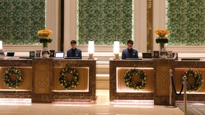 Taulell de recepció amb dos membres del personal, cadascú amb un portàtil, en un vestíbul decorat amb elements vegetals i guirlands al taulell.