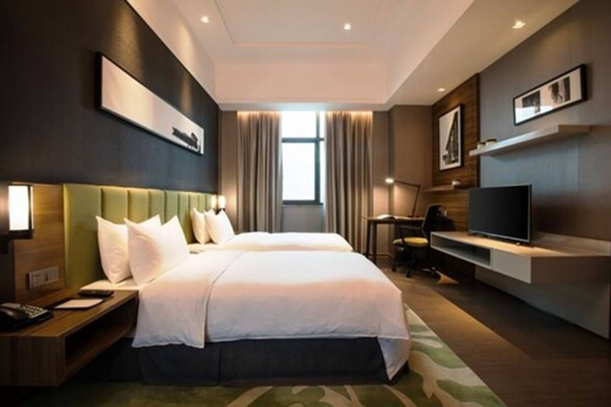 A hotel room with two beds, a desk, a television, and a large window with curtains.