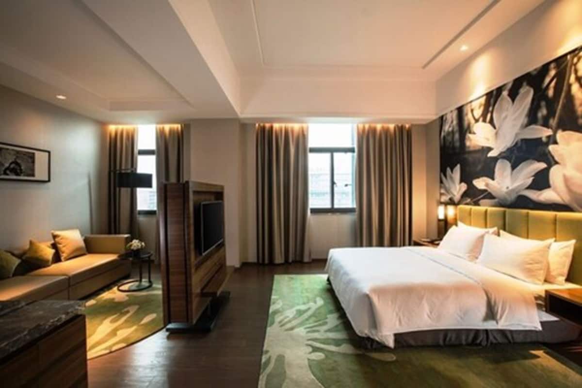 A modern hotel room with a large bed, a sofa, a TV, and a painting on the wall.