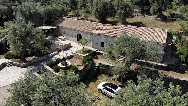 A stone building with a tiled roof, surrounded by trees and a car.