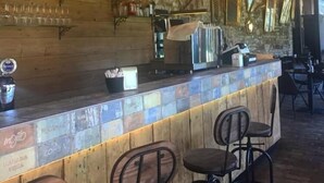 A rustic bar area with wooden shelves displaying bottles, a bicycle, and a bar counter with stools. - Il Vagabondo (Buttrio)