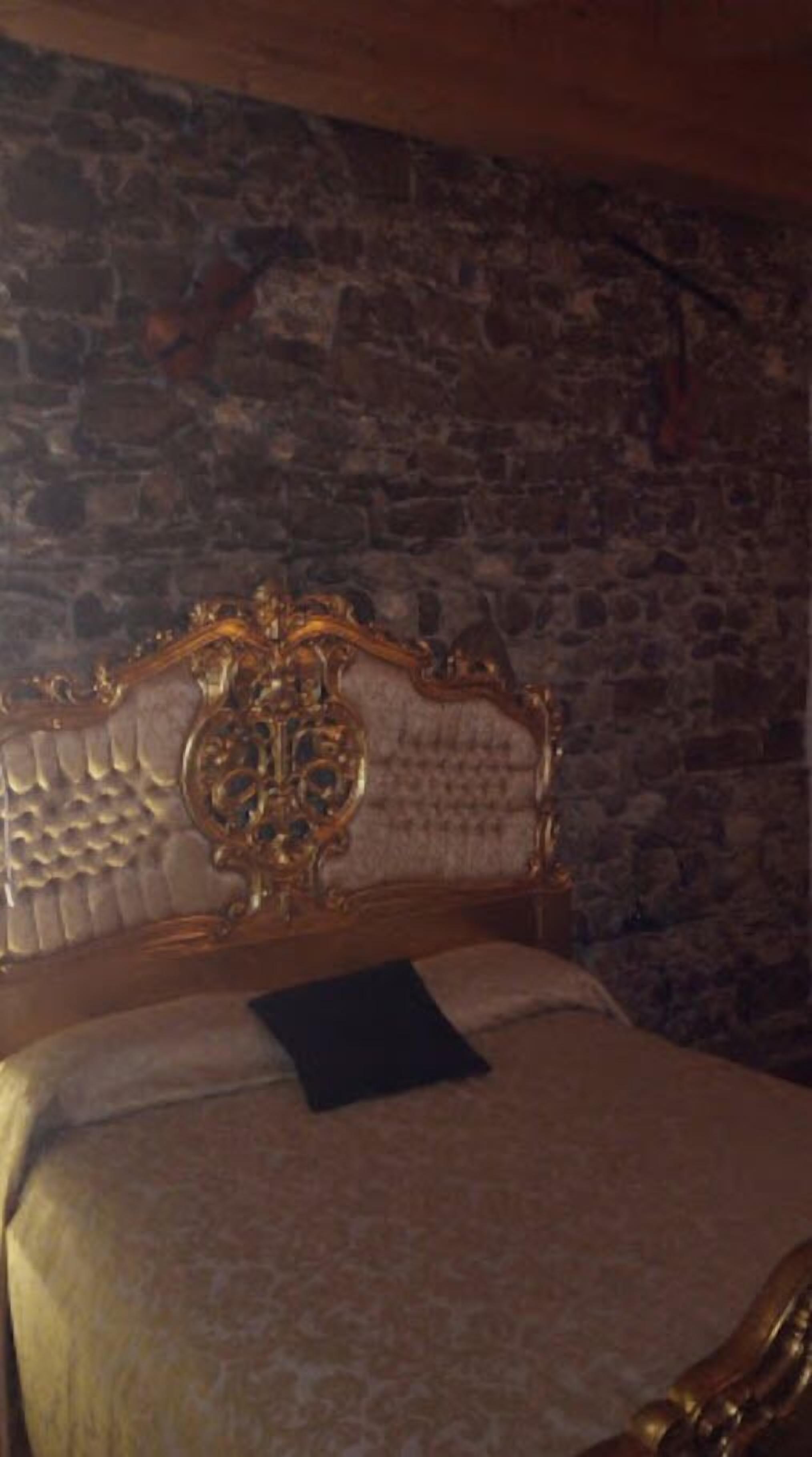 A bed with an ornate headboard in a room with stone walls.