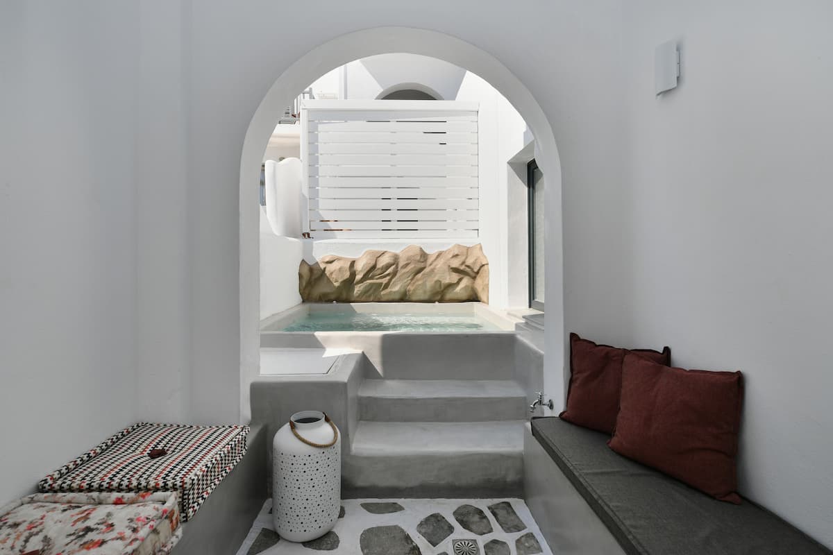 A modern, minimalist bathroom with a built-in bathtub, stone flooring, and a seating area with cushions.