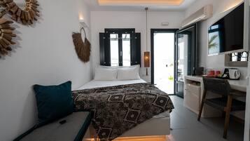 Un dormitorio moderno con cama, escritorio y silla. Hay una ventana con persianas, un televisor montado en la pared y una puerta que conduce a otra habitación.