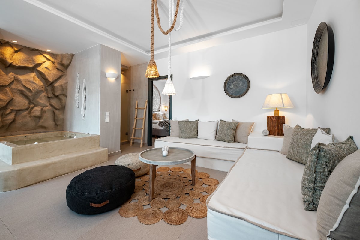 A modern living room with a stone wall, a sofa, a coffee table, and a small round table with a lamp.