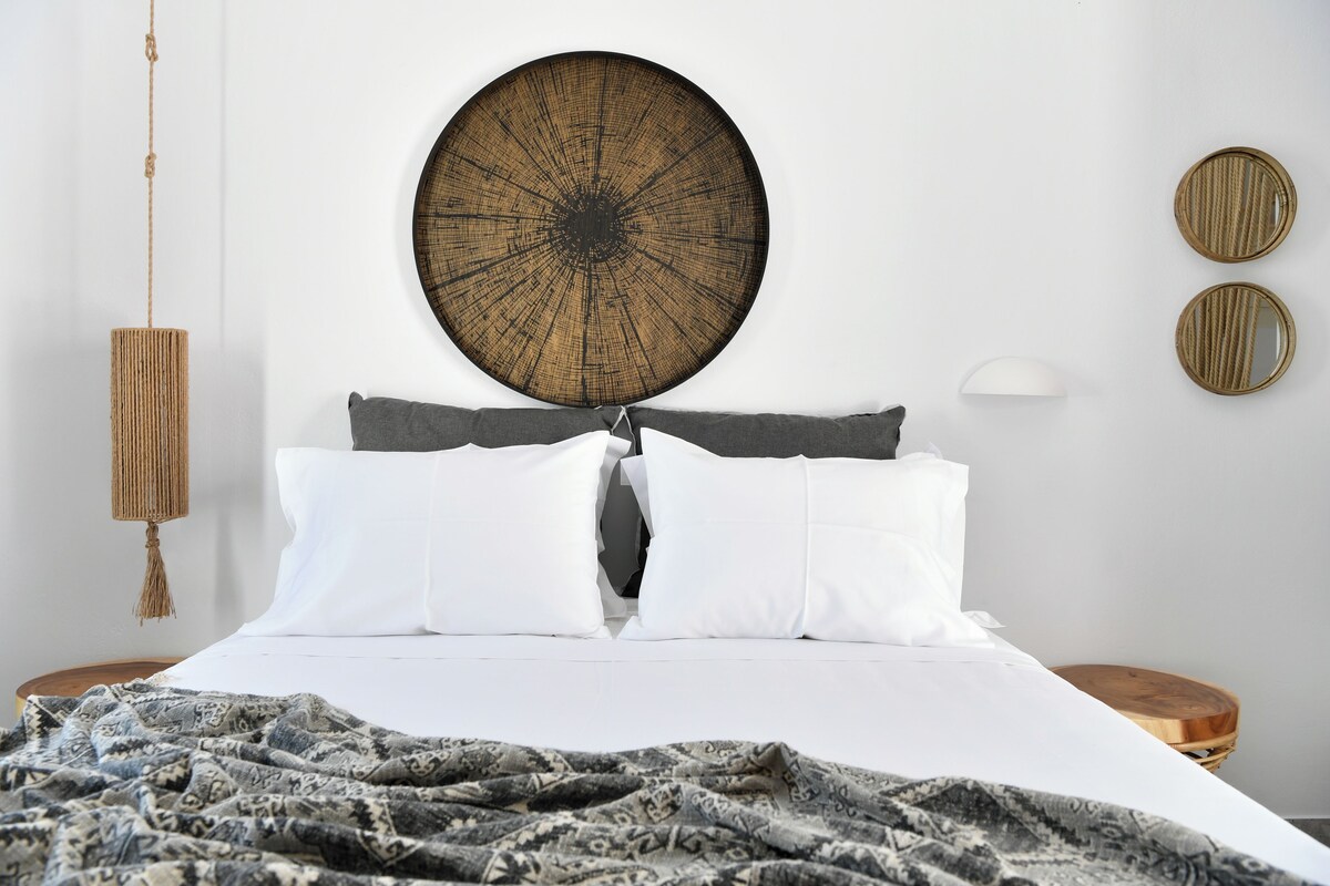 A neatly made bed with white and gray bedding, a large circular wall art above it, and two round mirrors on the wall.