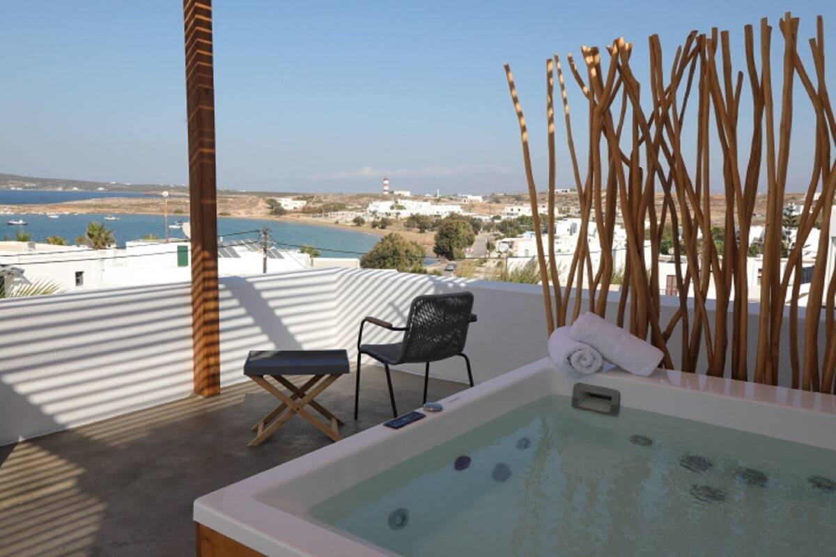 A rooftop terrace with a hot tub, a chair, and a view of the sea and buildings.