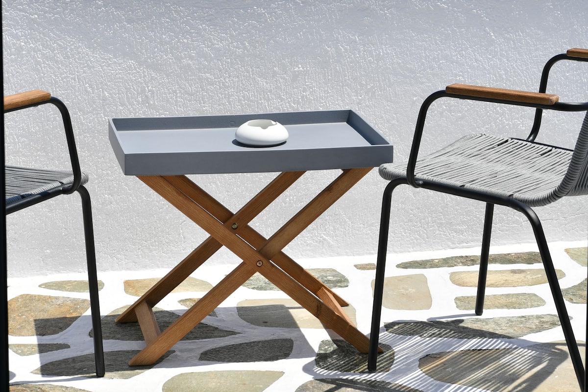 A terrace with a table and two chairs, overlooking a coastal landscape with buildings and a clear sky.