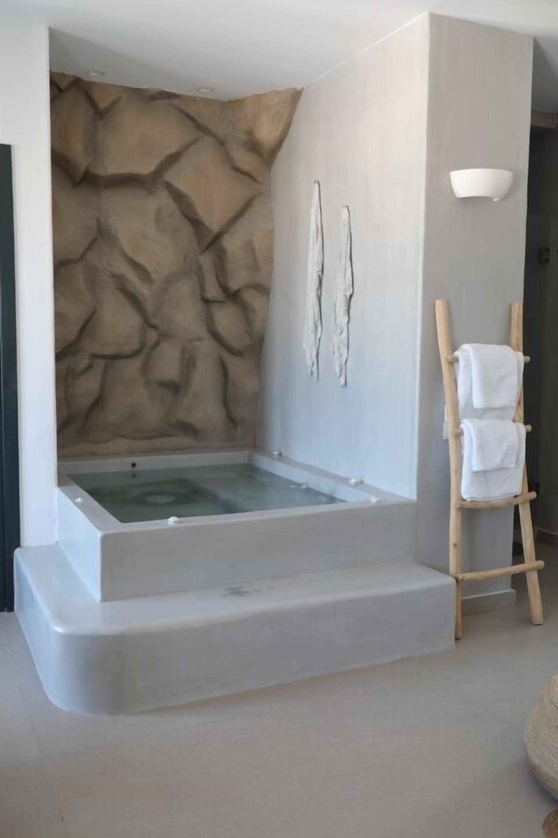 A modern bathroom with a stone-textured wall, a freestanding bathtub, and a wooden towel rack.
