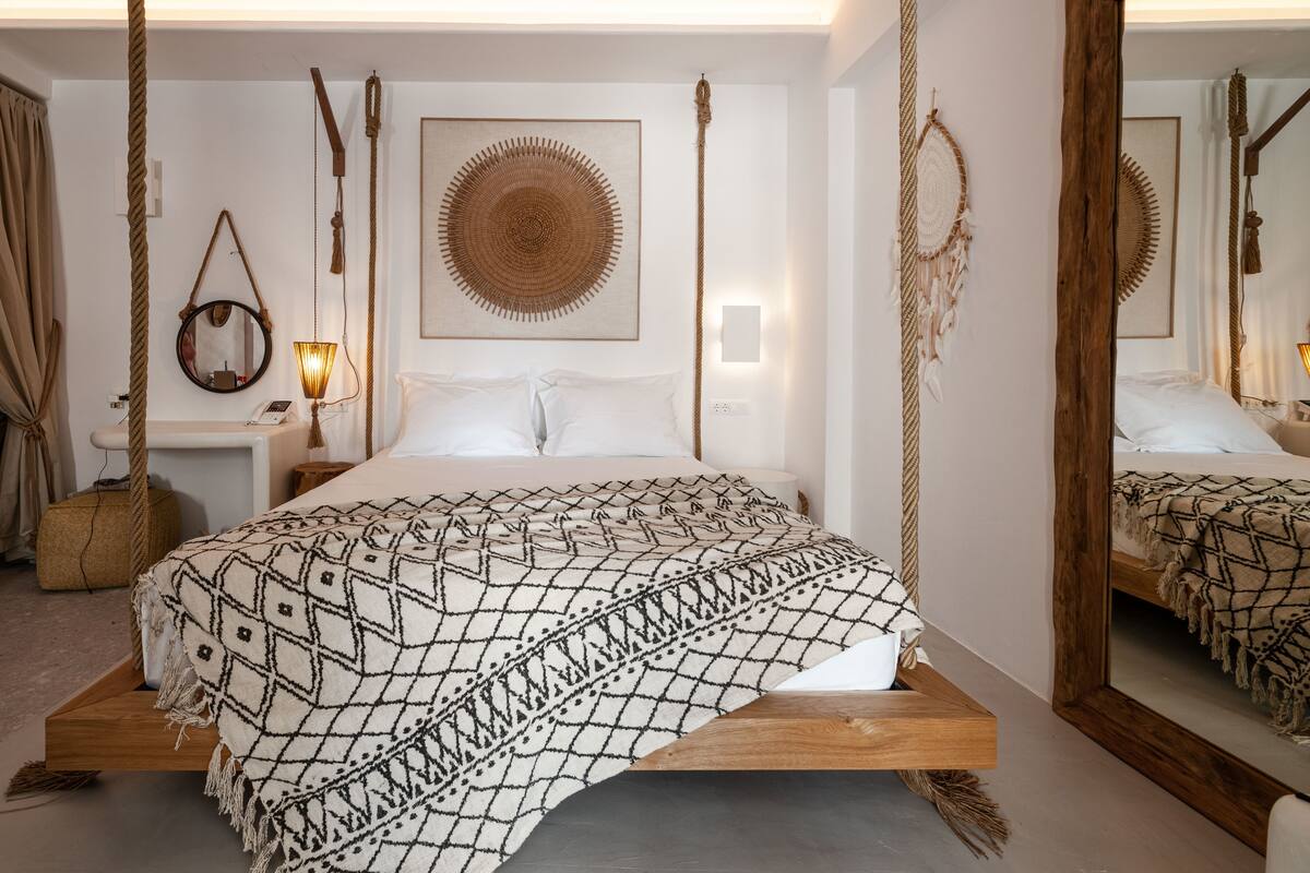 A bed with a geometric patterned blanket, a hanging rope, a woven wall hanging, and a mirror.