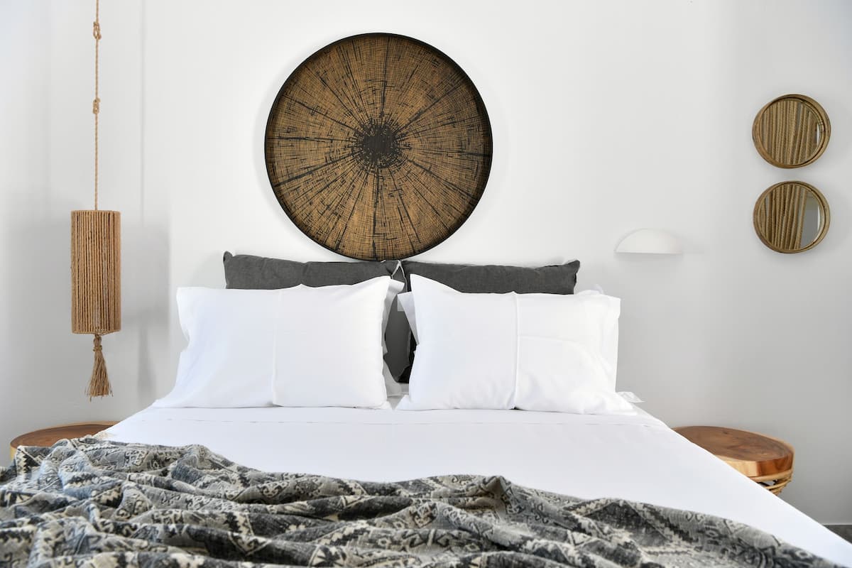 A neatly made bed with white linens, a patterned throw blanket, and a large circular wall art piece above it.