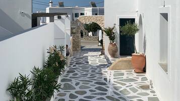 Un callejón estrecho, con paredes blancas y suelo de piedra, que conduce a un arco de piedra y un edificio con una puerta oscura.