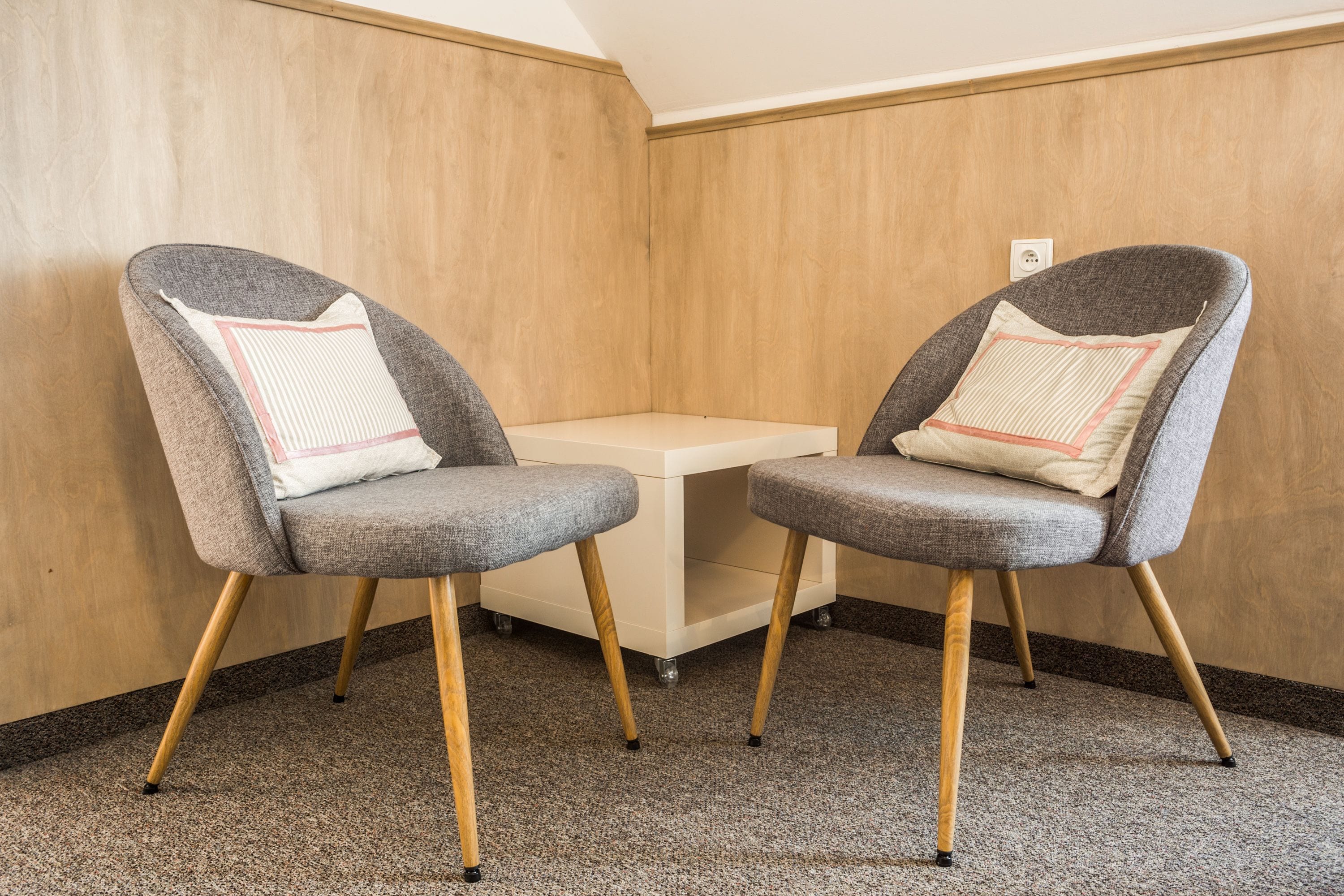 Two grey upholstered chairs with wooden legs and a small table between them.