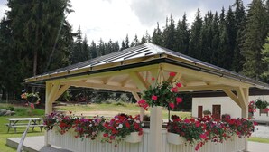A covered pavilion with a wooden roof, surrounded by flower planters. - Penzion Bílá voda (Harrachov)