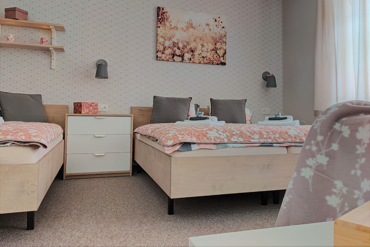 A hotel room with two beds, a nightstand, a dresser, a wall-mounted lamp, and a floral artwork.