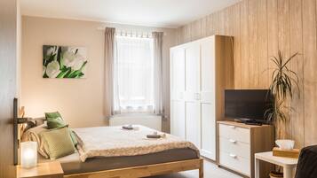 Ein Schlafzimmer mit Bett, Fernseher, Kleiderschrank, einem Fenster mit Vorhängen und einem Bild an der Wand.