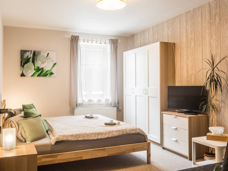 Ein Schlafzimmer mit Bett, Fernseher, Kleiderschrank, einem Fenster mit Vorhängen und einem Bild an der Wand.