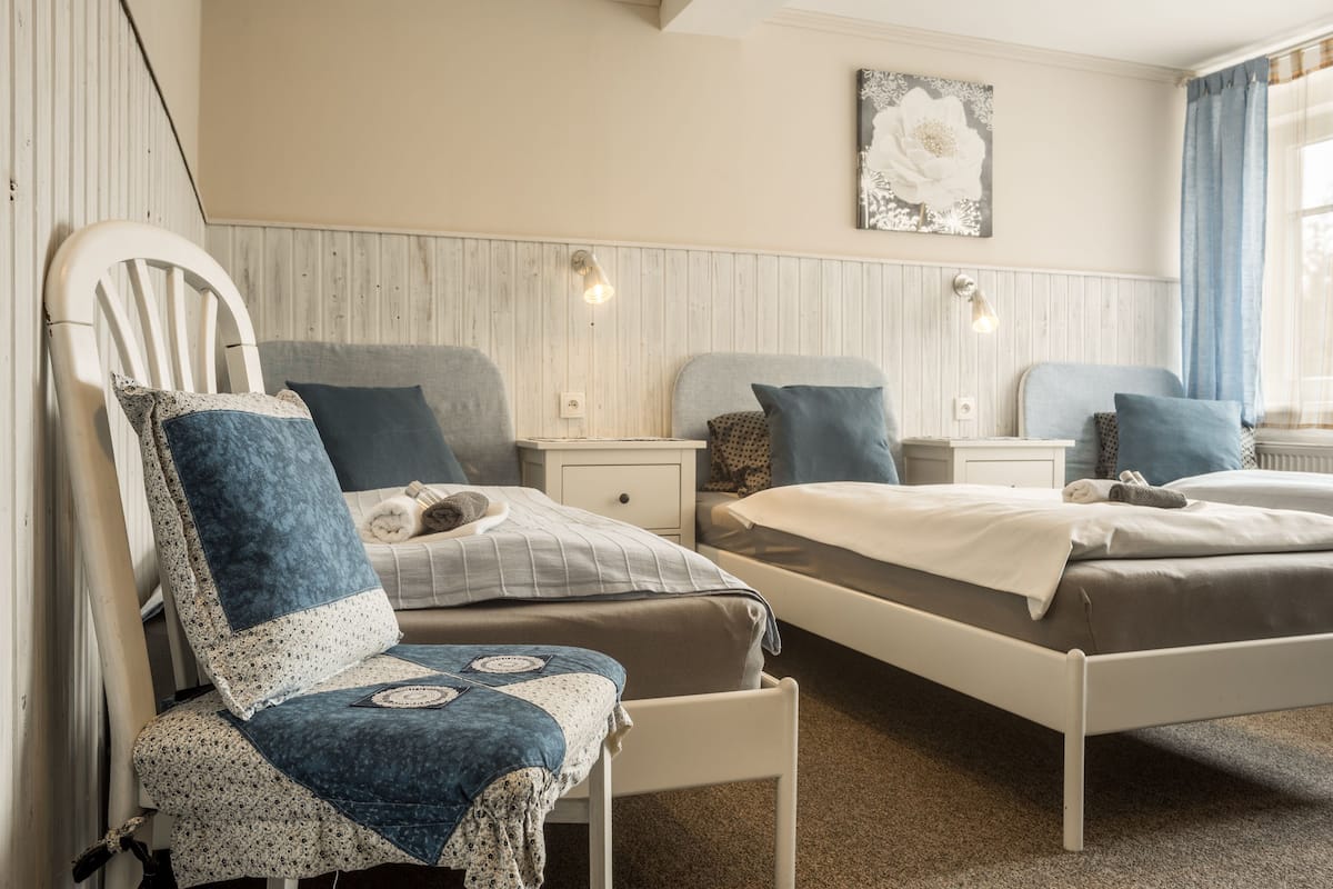 A bedroom with two beds, a nightstand, a chair, and a wall-mounted light fixture.