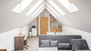 A modern loft bedroom with a skylight, a gray sofa, a wooden desk, and a kitchenette. - Penzion Bílá voda (Harrachov)