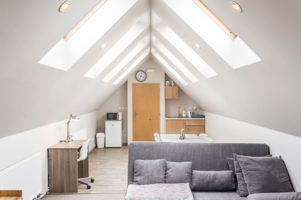 A modern loft bedroom with a skylight, a gray sofa, a wooden desk, and a kitchenette.